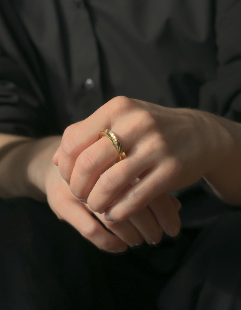 Two-piece gold ring with a polished surface, worn on the middle finger of the left hand