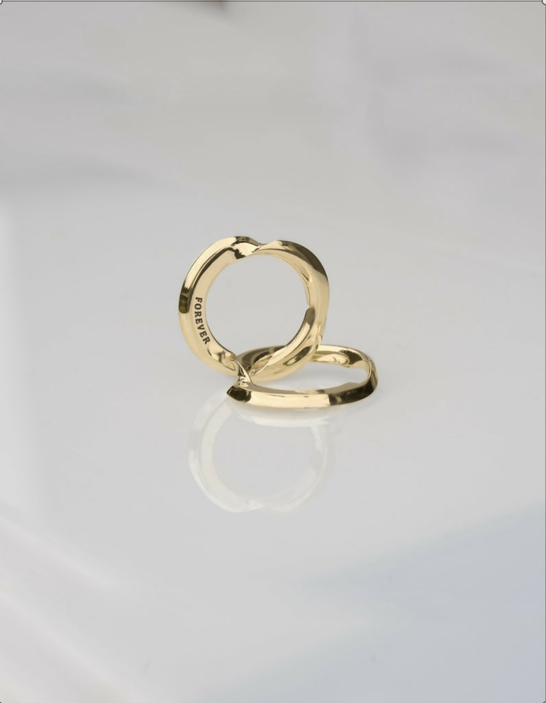 Two-piece gold ring with a polished surface, opened, one half lying down, the other standing upright, the hidden inner surfaces offer space for individual engraving