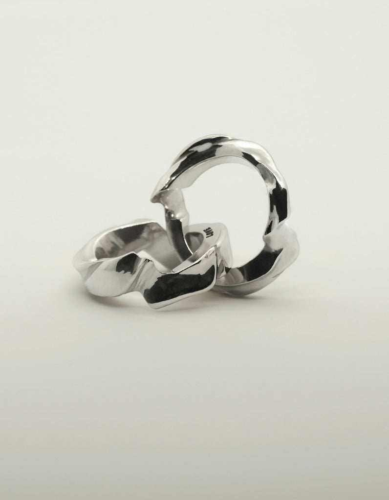 Two-part silver ring with a polished surface, opened, one half lying down, the other half standing upright. The hidden inner surfaces offer space for individual engraving