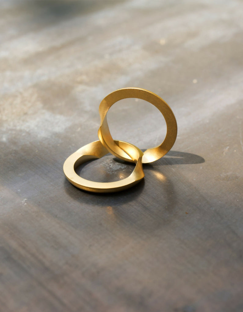 Two-part ring made of gold with a matt surface, opened, one half lying down, the other half standing upright. Individual engraving can be seen on the hidden inner surfaces.