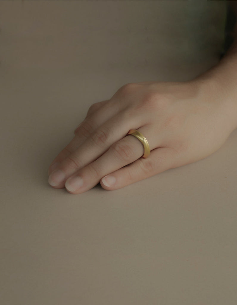 Two-piece gold ring with a matt surface, worn on the middle finger of the left hand.