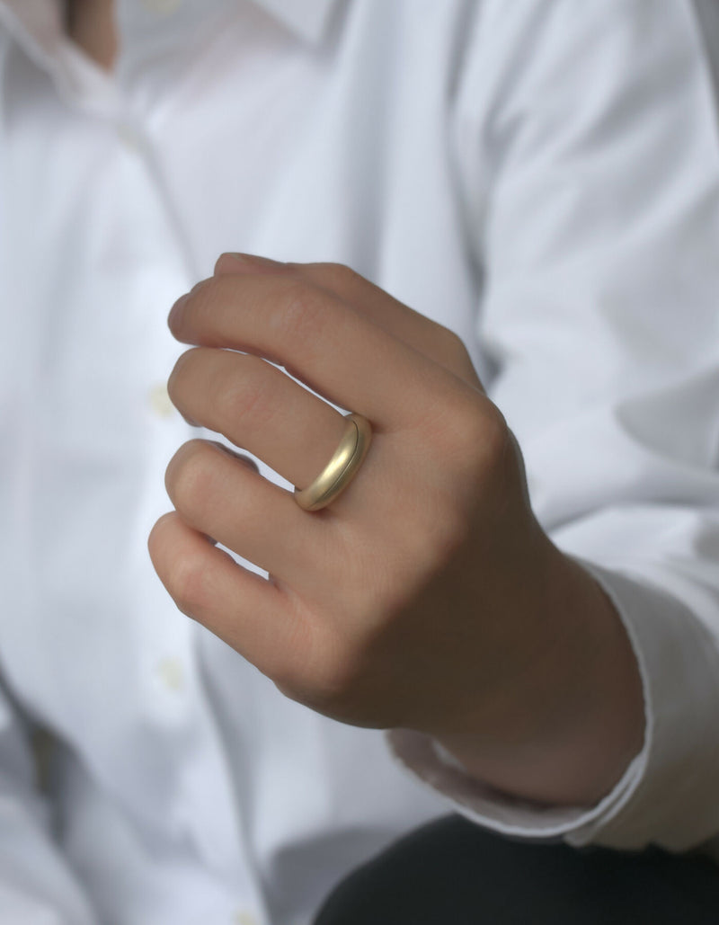 Two-piece ring made of gold with a matt surface, worn on the middle finger of the left hand.