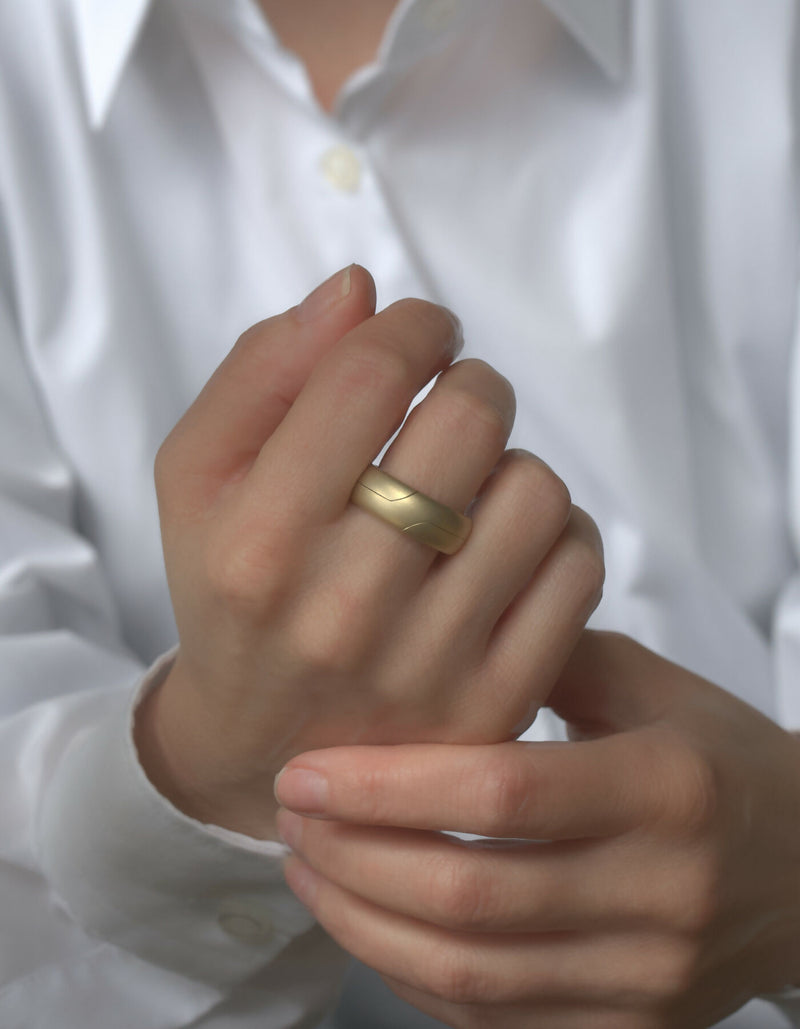 Two-piece gold ring with a matt surface and an oval cross-sectional profile, worn on the middle finger of the left hand.