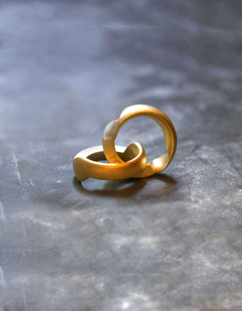 Two-part gold ring with a matt surface and an oval cross-sectional profile, opened, one half lying down, the other half standing upright. The hidden inner surfaces offer space for individual engraving