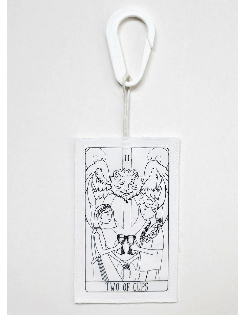 THE TWO OF CUPS tag is made from leftover deadstock white cotton poplin. The black and white tag has an exclusive design inspired by tarot cards drawn by the artist Maria Robla and is printed in collaboration with RoStudio. Wear the tag alone or attach it to the essential pieces to personalize them. The tag is sold with key holder in recycled plastic made in collaboration with Samji Atelier. White Canvas x Maria Robla.